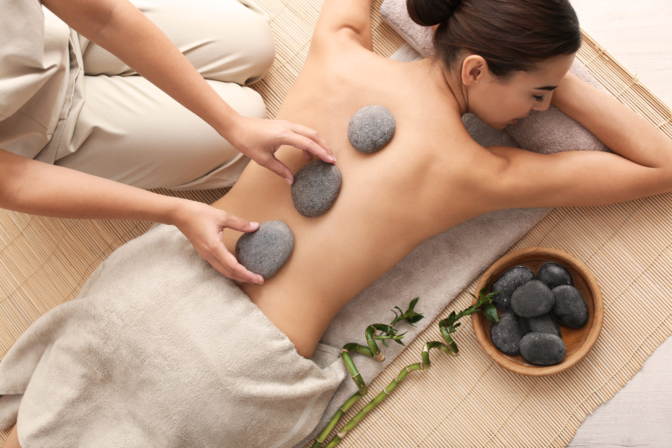 Beautiful young woman getting hot stone massage in spa salon, top view
