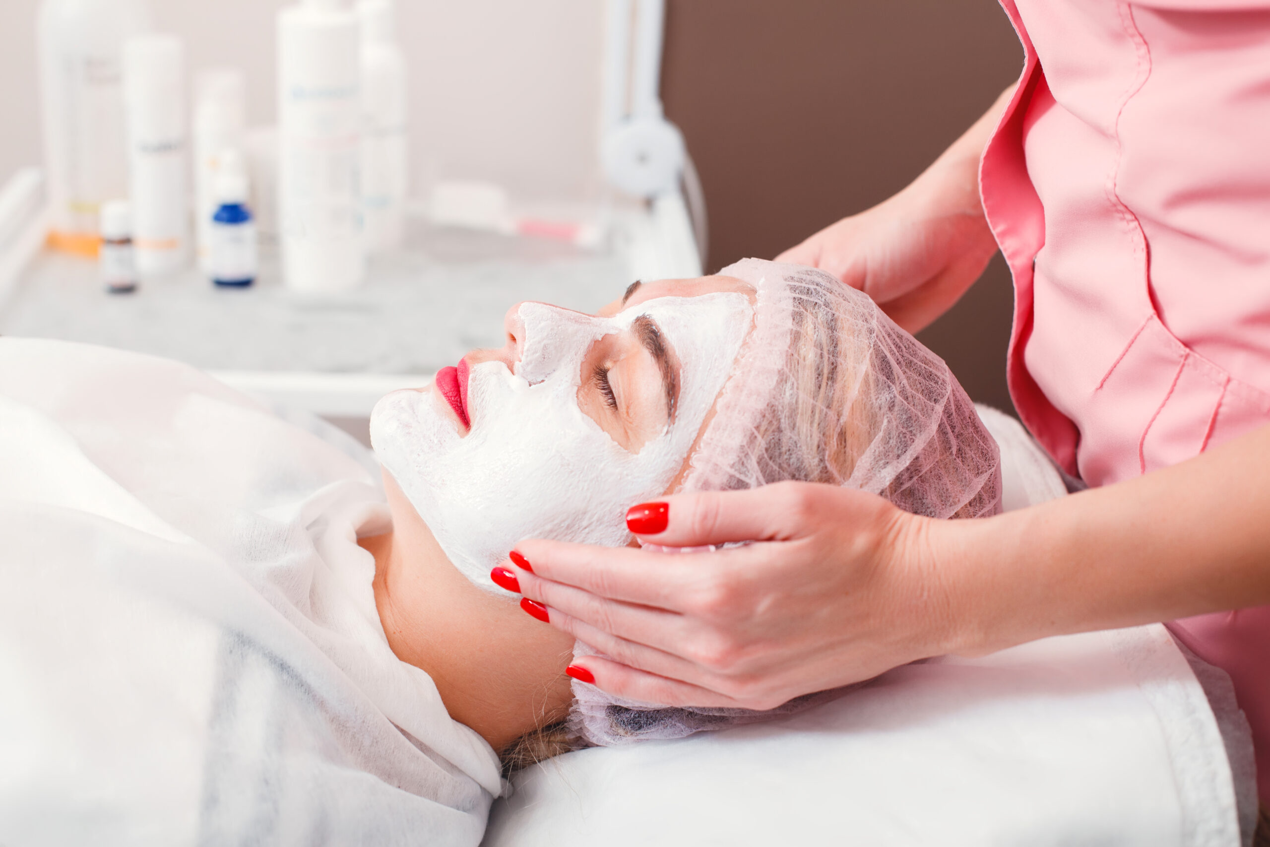 Beautician apply facial cream on young woman face skin. Cosmetic procedure in spa salon. Mask for facial skin care