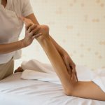 Close Up of massage therapist massaging female leg at spa salon.