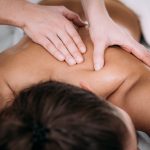 Physiotherapist massaging female patient with injured shoulder blade.  Sports injury treatment.